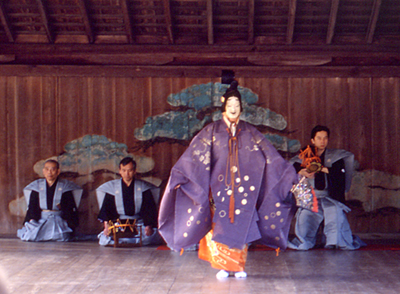 This is an image of a Noh actor; behind him is a group of stage musicians.