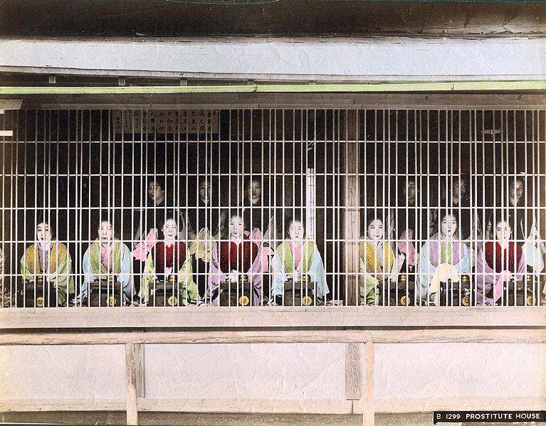 This is a colorized photo of prostitutes on display to patrons in Edo period Japan. the use of the bamboo cage behind which to display them was eventually banned (though the practice of prostitution would remain legal until after World War II).